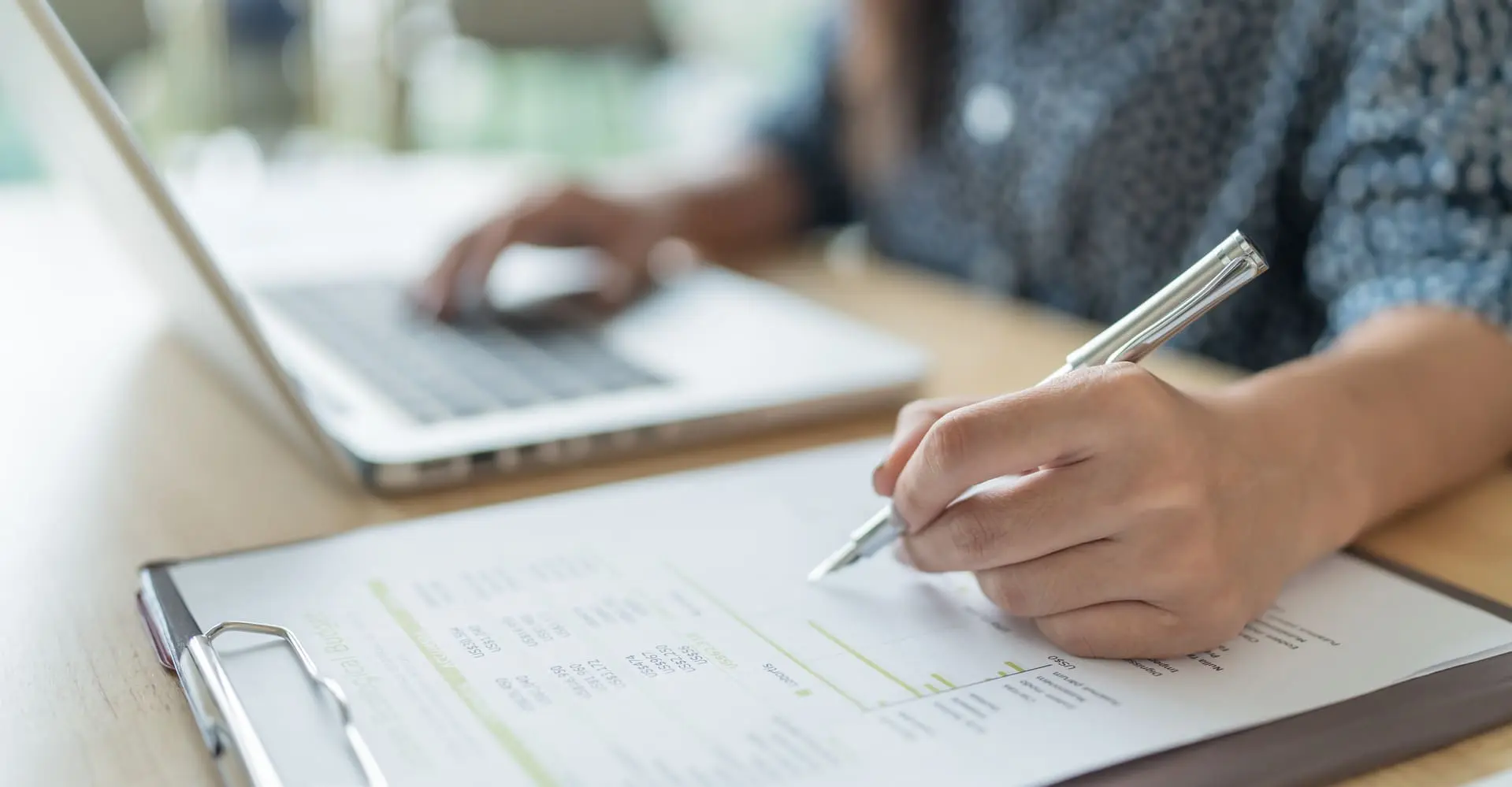 Personne remplissant un formulaire sur un papier et travaillant sur son ordinateur